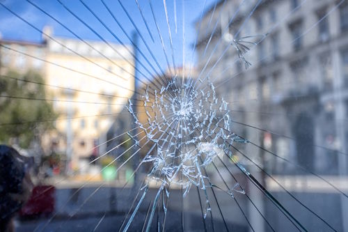Cracked glass at a hotel entrance after vandalism, illustrating physical damage and security risks for hotel owners.
