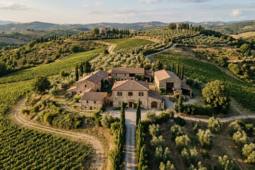 Italian countryside estate with multiple stone buildings surrounded by vineyards and olive groves in rural Italy