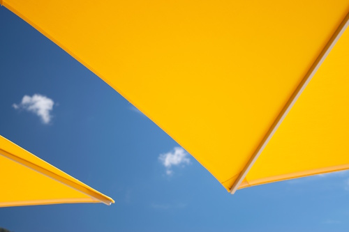 Yellow sunshades against a clear blue sky, symbolizing heat protection and summer adaptation in hospitality