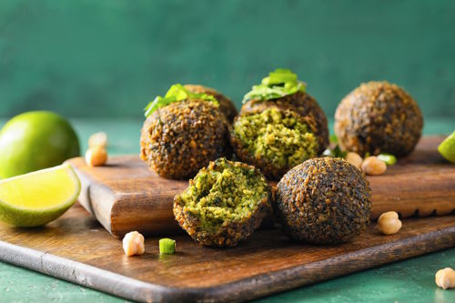 Plant-based falafel made from chickpeas served on a wooden board with fresh herbs and lime